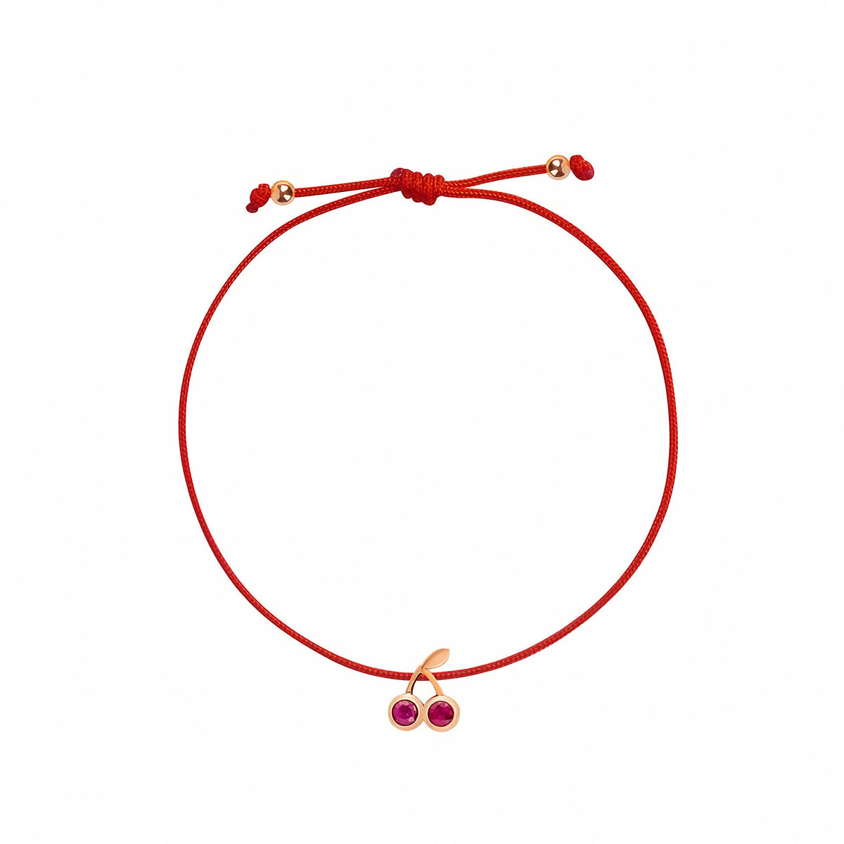 Rosmundo collaboration 18k rose gold cherry string bracelet with natural rubies on adjustable macrame cordA red cord bracelet with an adjustable knot and a small rose gold-tone cherry charm featuring two pink gemstones, shown on a plain white background.