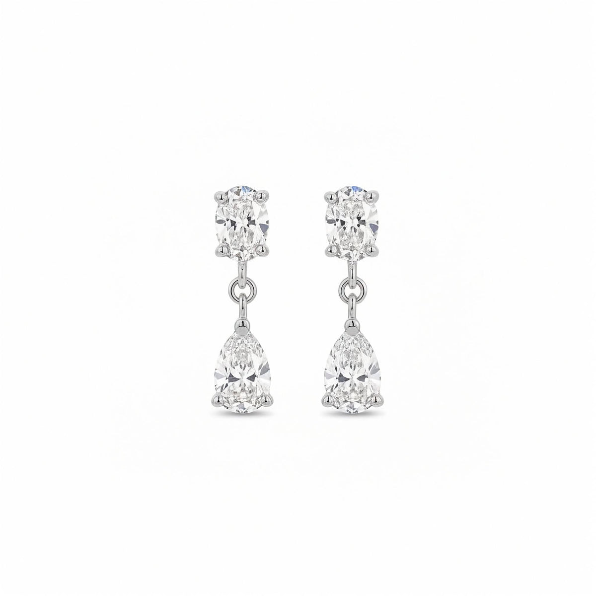 14k white gold drop earrings with 3.00 ctw upright oval studs and dangling pear-cut lab diamonds. A pair of white gold drop earrings featuring a oval-cut lab grown diamonds in a prong setting on the top and a pear-cut clear gemstone in a prong setting below, shown against a plain white background.