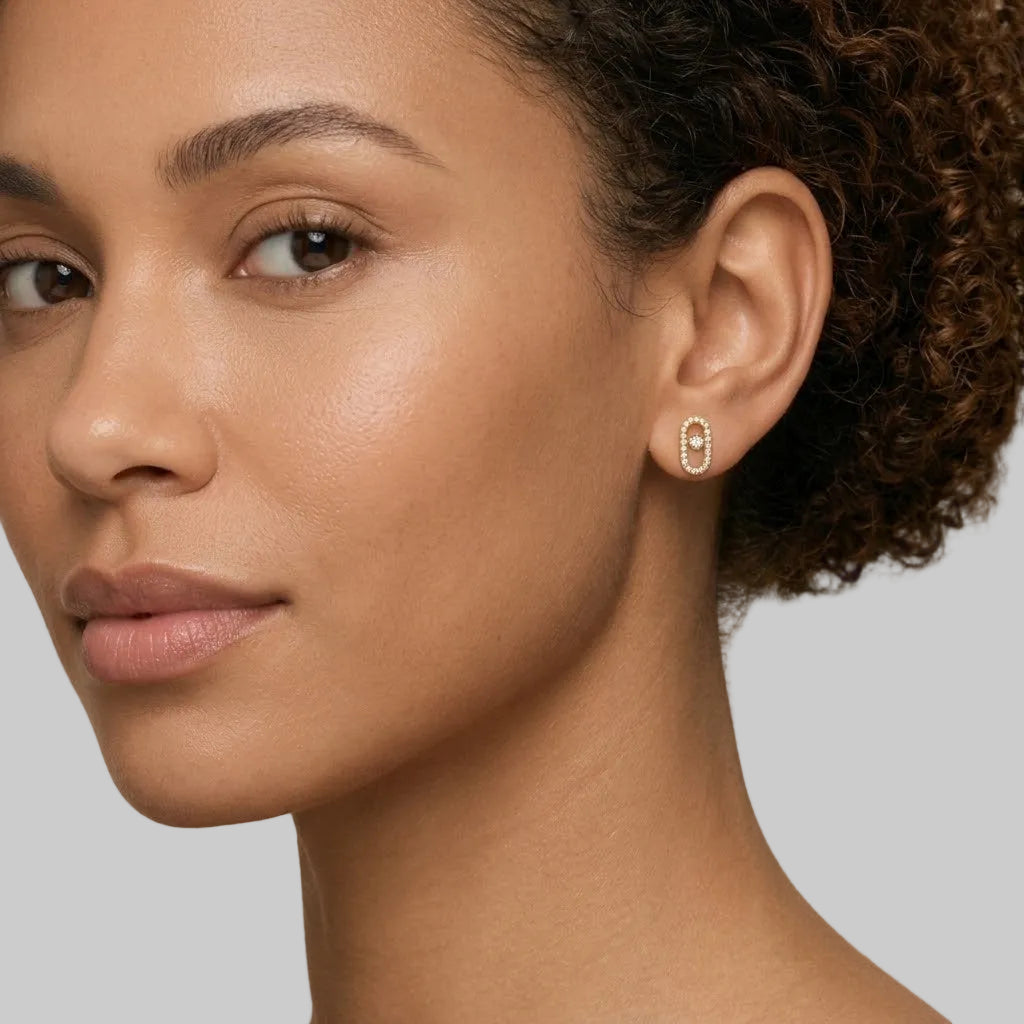Close-up view of 14k gold elongated oval frame stud featuring round bezel diamond center and pave halo  shown on the model.