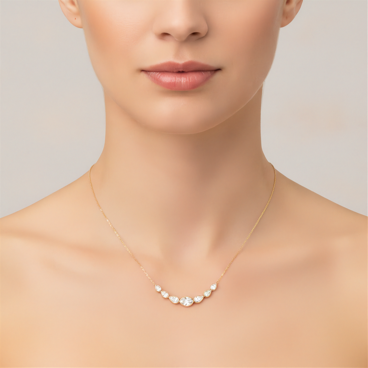 14K yellow gold curved bar necklace with center oval diamond and graduated pear diamonds by Inga Fine Jewelry shown on model on light gray background.