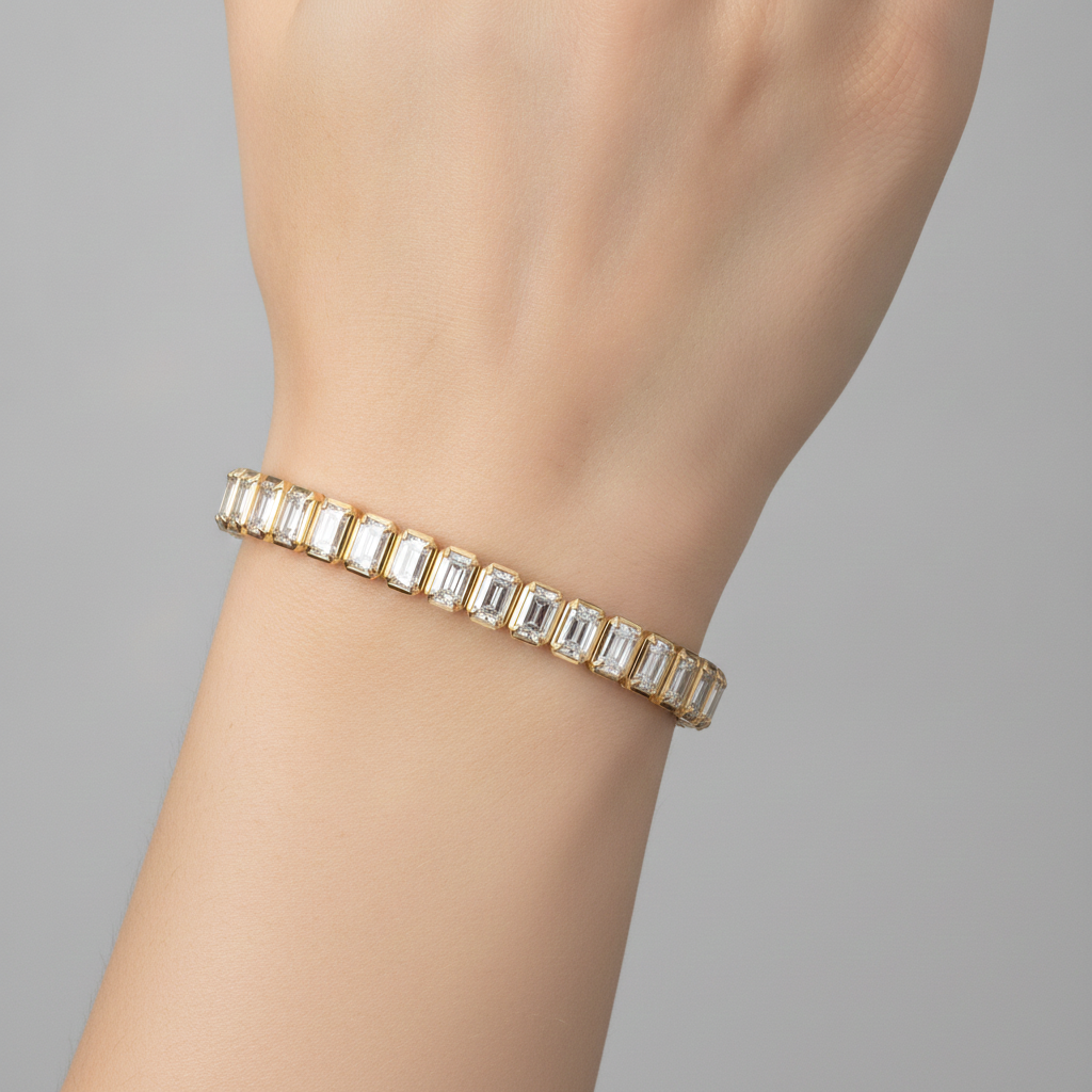 14K yellow gold bezel set emerald cut lab grown diamond tennis bracelet 9.92 ctw Inga Fine Jewelry on the model and gray backgound.