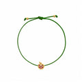 Rosmundo collaboration 18k yellow gold apple string bracelet with natural rubies and diamond on adjustable macrame cord. A green adjustable cord bracelet featuring a small yellow gold apple charm embellished with purple gemstones, set against a plain white background.