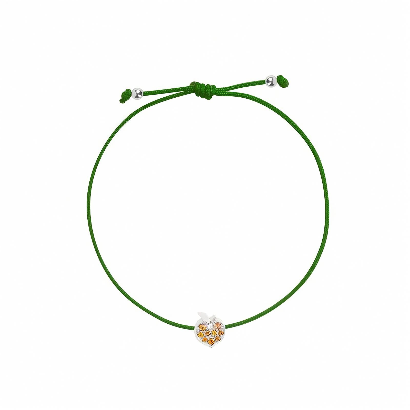 Rosmundo collaboration 18k white gold peach string bracelet with natural orange sapphires and diamond on adjustable macrame cord. A green adjustable cord bracelet featuring a small apple-shaped charm with white gold and orange details, displayed on a clean white background.