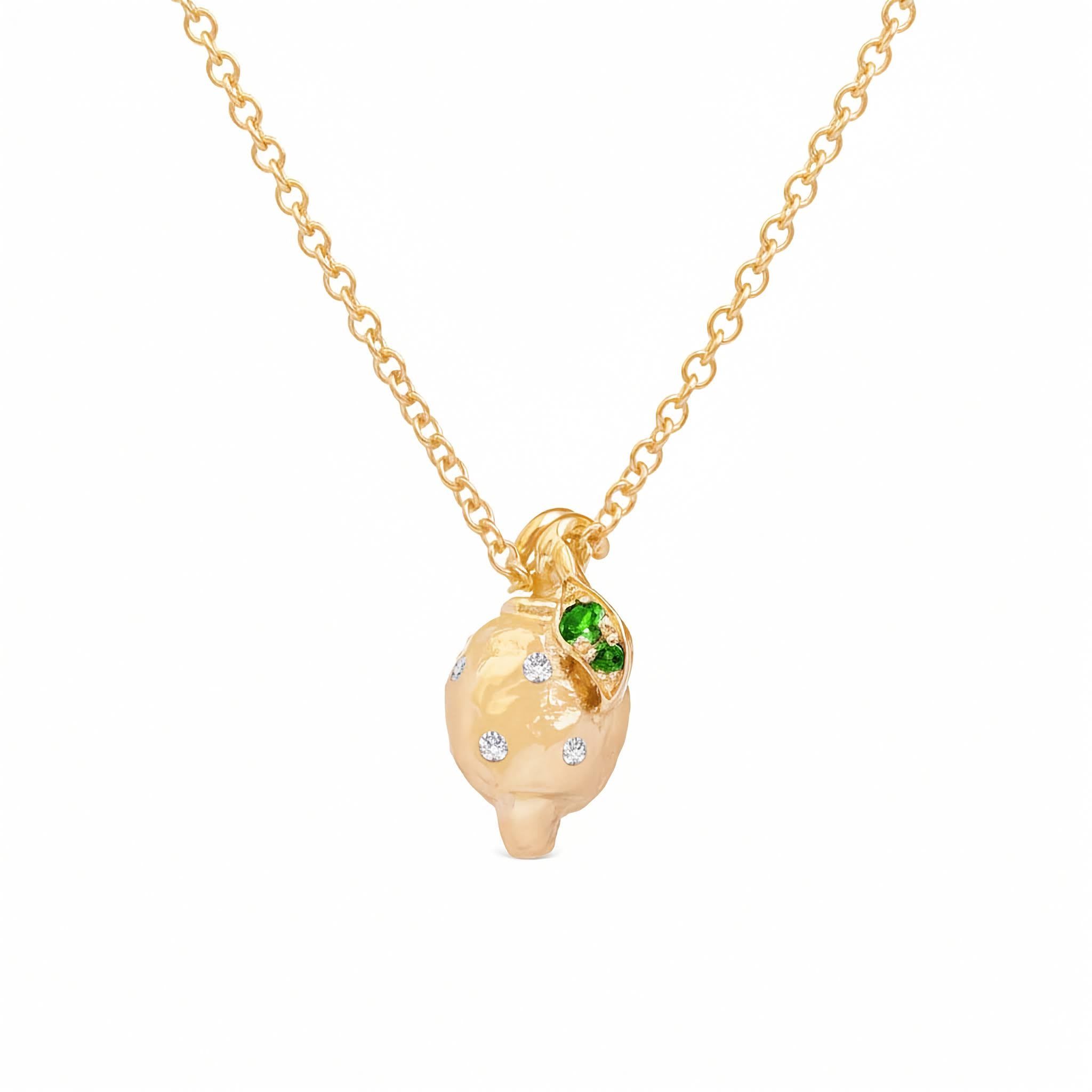 A gold pendant necklace featuring a stylized, textured lemon pendant with small white diamonds and a green emerald color accent gemstones, shown on a white background.