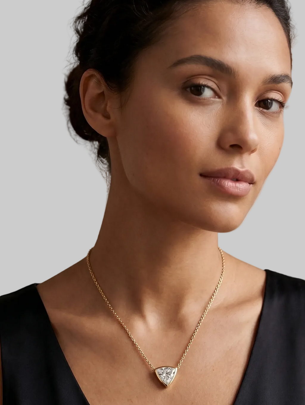 A yellow gold necklace with a delicate chain and a triangular pendant featuring a clear trilliant - cut diamond, shown on a model.