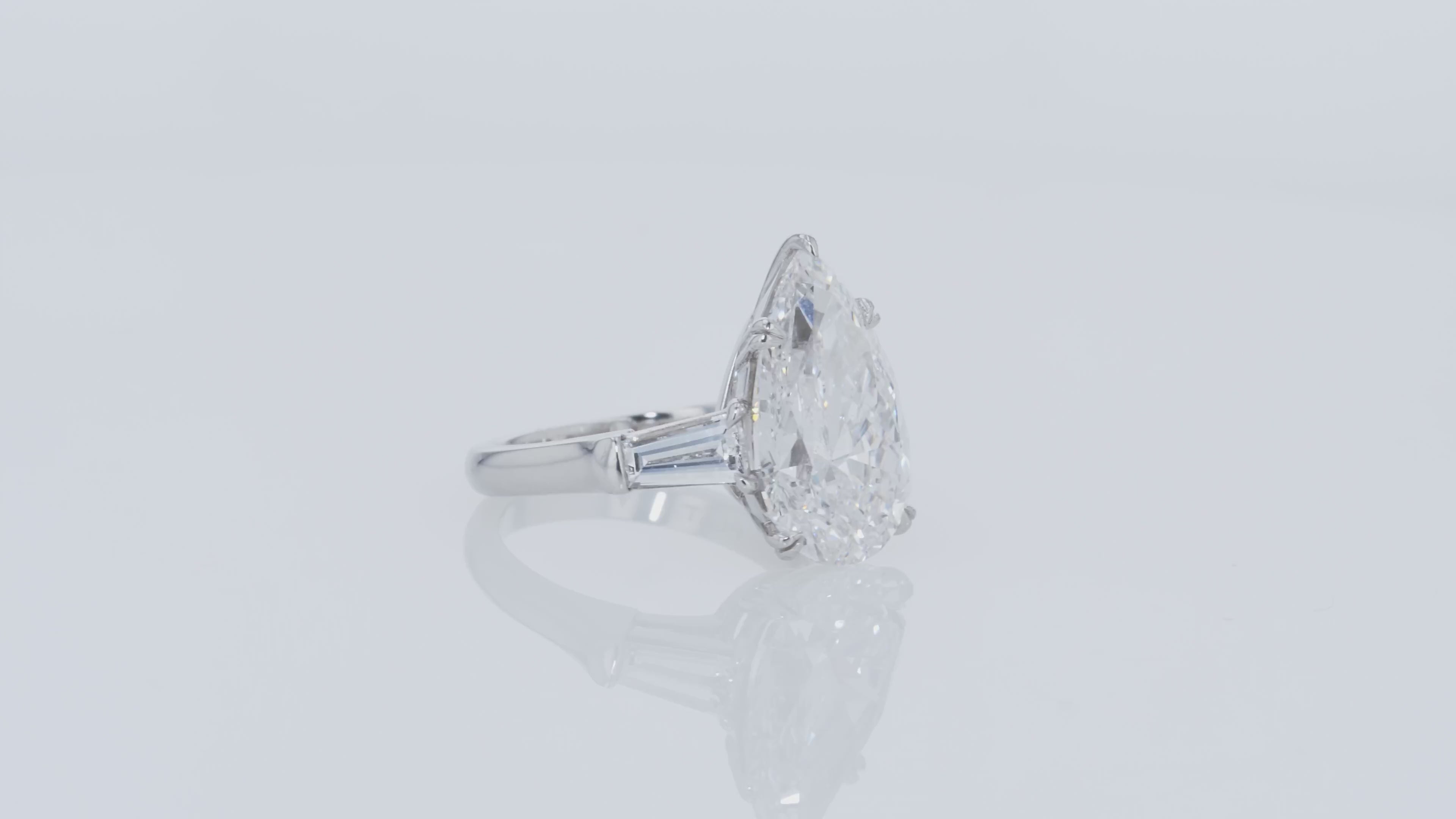 Video of a diamond ring with pear-shaped center stone and tapered baguettes side diamonds on a gray background.
