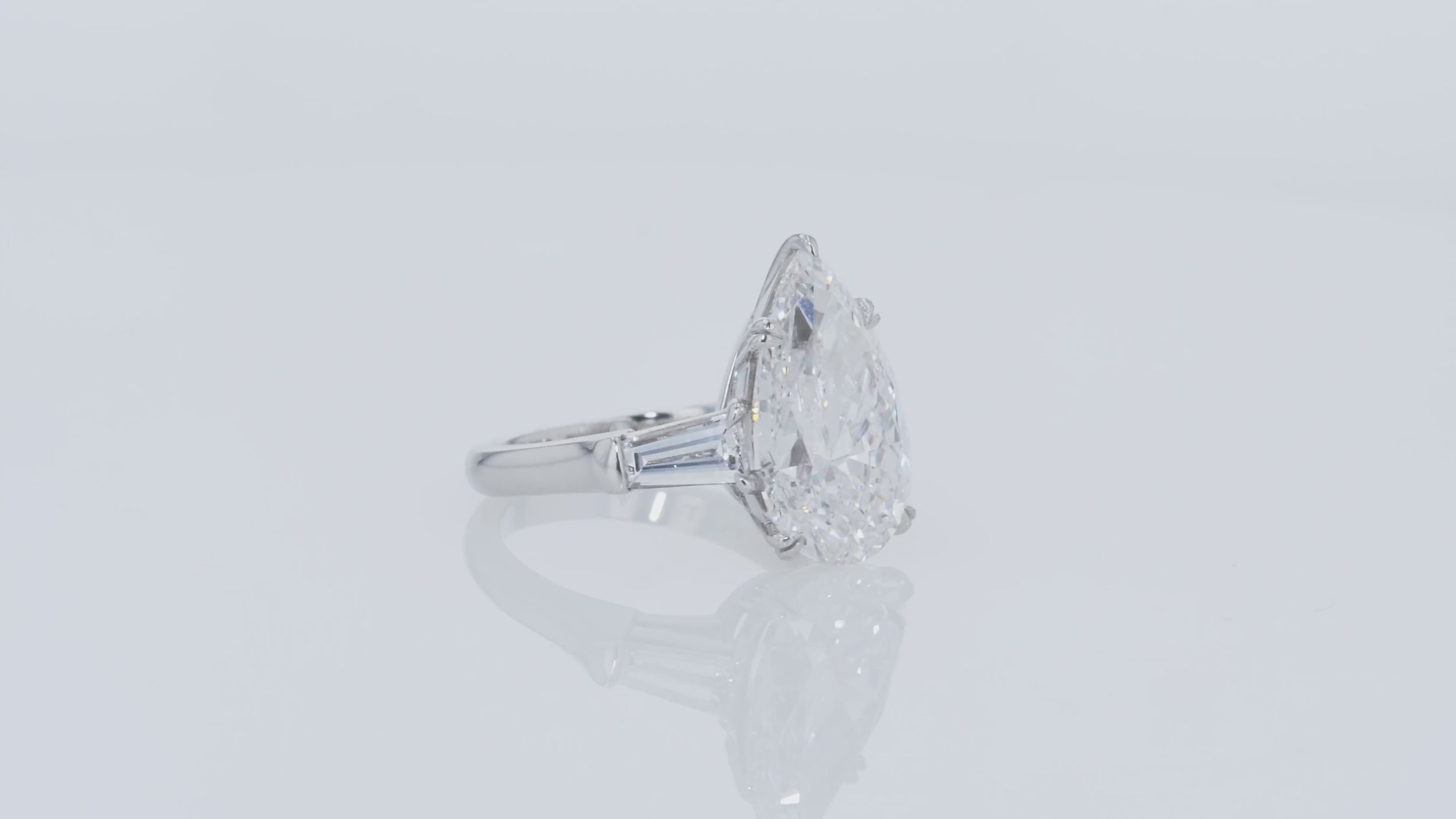 Video of a diamond ring with pear-shaped center stone and tapered baguettes side diamonds on a gray background.