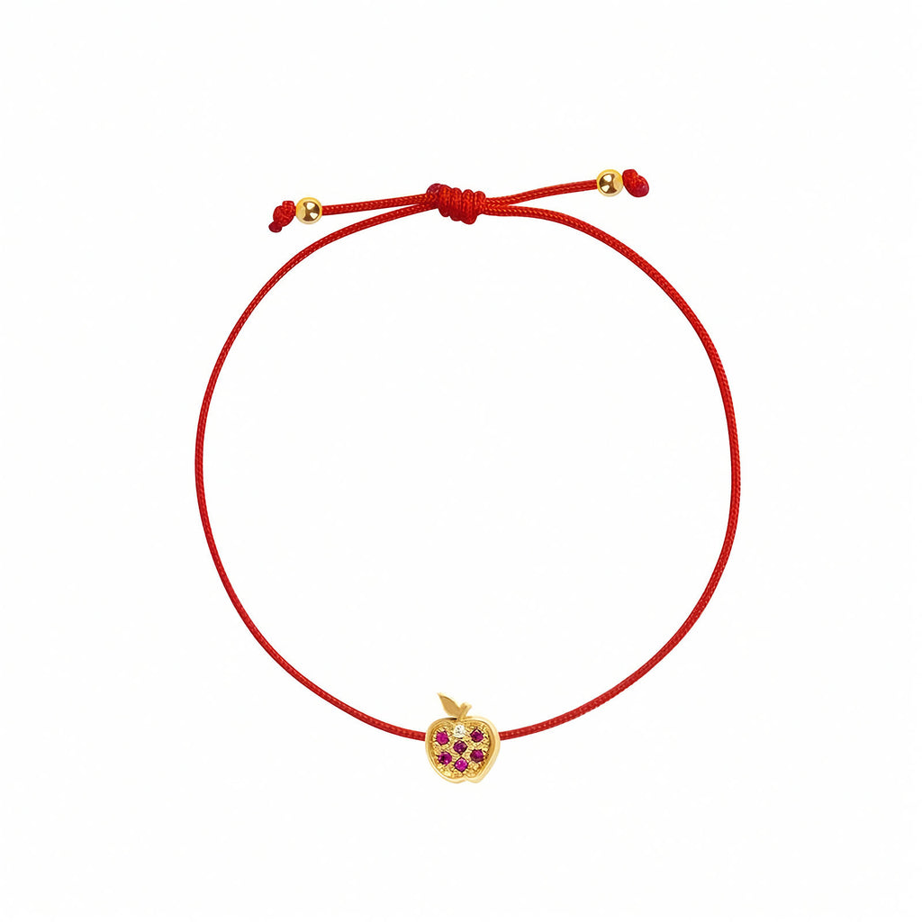 Rosmundo collaboration 18k yellow gold apple string bracelet with natural rubies and diamond on adjustable macrame cord. A red adjustable cord bracelet featuring a small yellow gold apple charm embellished with purple gemstones, set against a plain white background.