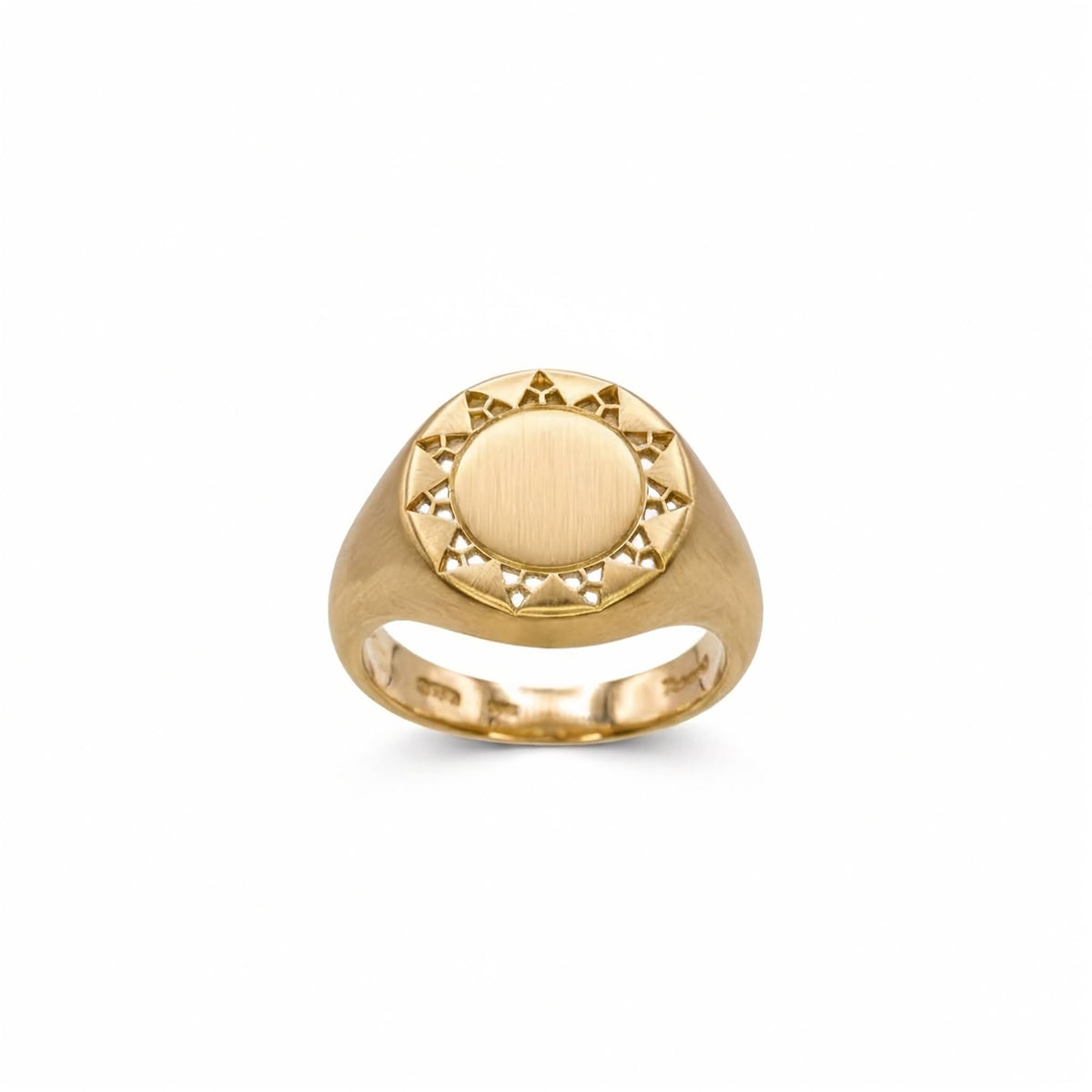 A yellow gold signet ring with a circular sunburst design on the face, featuring a brushed center and small cutout details around the border, shown on a plain white background.