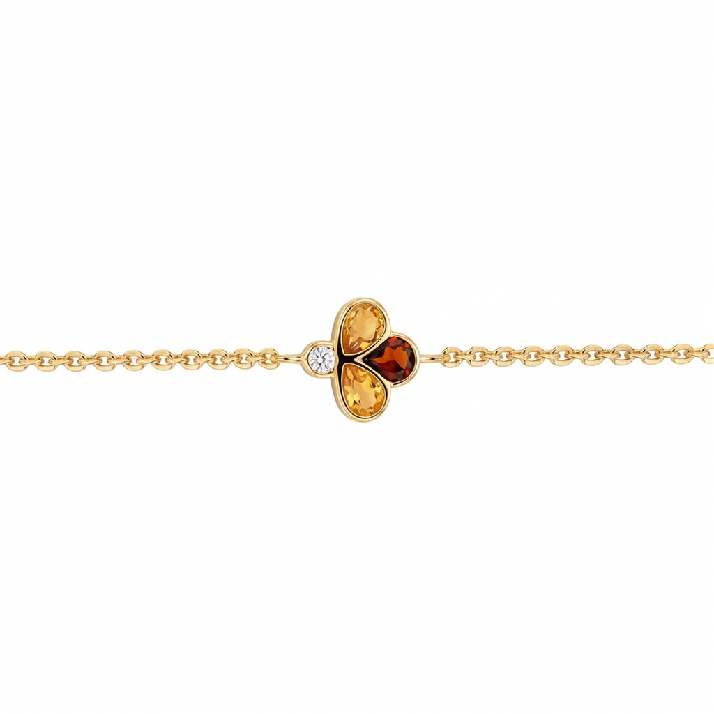 A delicate yellow gold chain bracelet featuring a central clover-like charm with two yellow gemstones, one amber-orange gemstone, and a small clear accent diamond, shown on a plain white background.