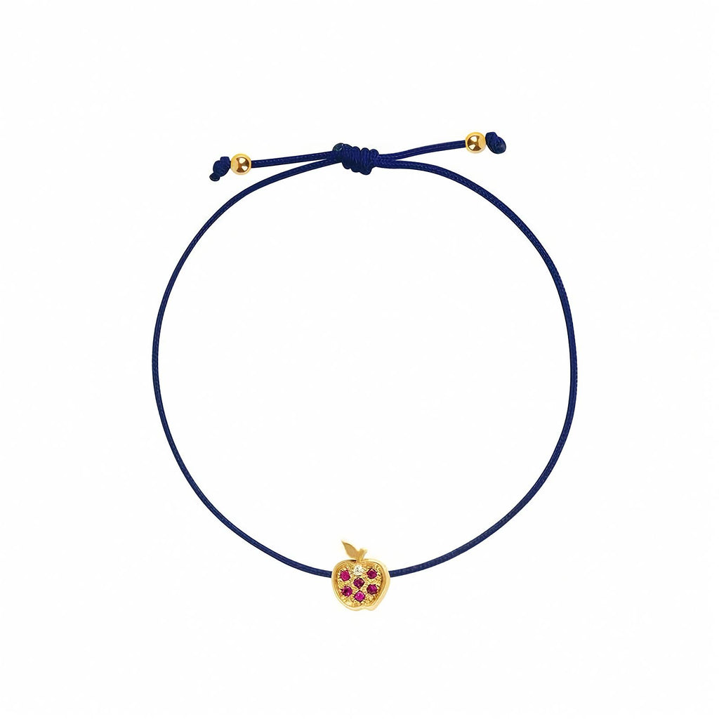 Rosmundo collaboration 18k yellow gold apple string bracelet with natural rubies and diamond on adjustable macrame cord. A blue adjustable cord bracelet featuring a small yellow gold apple charm embellished with purple gemstones, set against a plain white background.